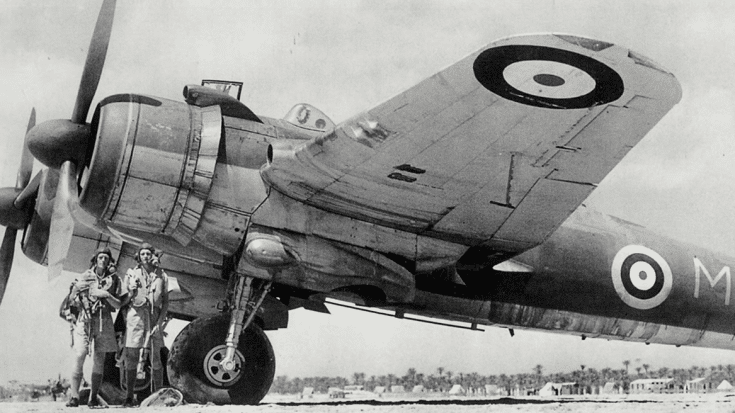 A Bristol Beaufighter parked on an airfield, with two uniformed crew members standing beside its wing.